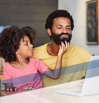 Father looking at laptop while daughter plays with his beard